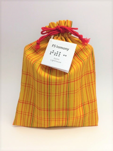 黄色い着物地で、赤い紐の巾着。トモニーの商品タグが付いています。